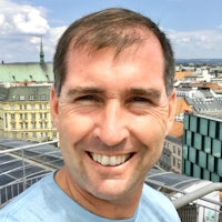 a man smiling on a rooftop with a city in the background